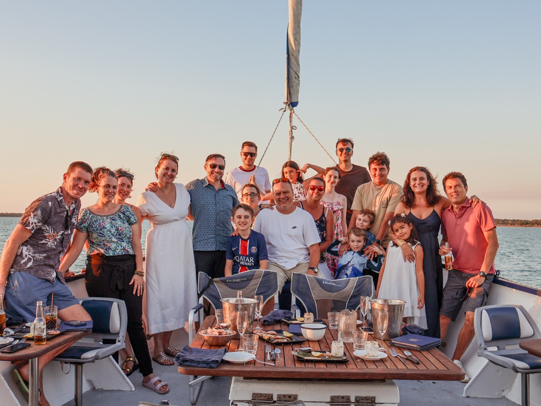 A large group gathered on deck around a set table for a sunset event aboard Cape Adieu